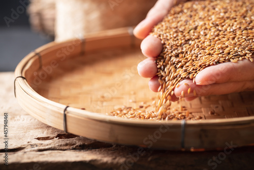 Brown flax seed holding by hand and pouring on bamboo tray