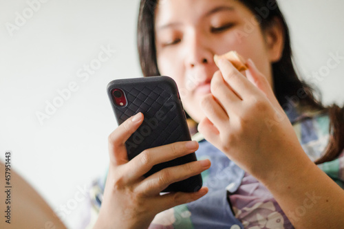 Closeup image of a beautiful young asian woman holding and using mobile phone at home
