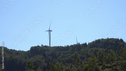 Massive wind turbines rotating on top of hill at island Fitjar in Norway - Static with pollen flying around in lush greenery area during summer