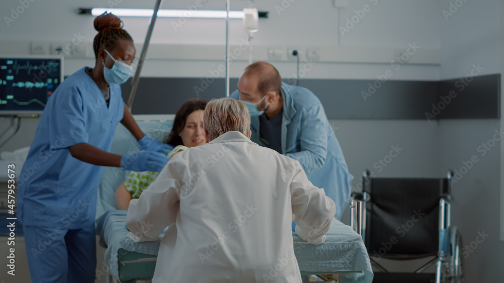 Obraz premium Obstetrics doctor and african american nurse delivering child in hospital ward at maternity. Caucasian pregnant woman with painful contractions pushing for childbirth with father of child