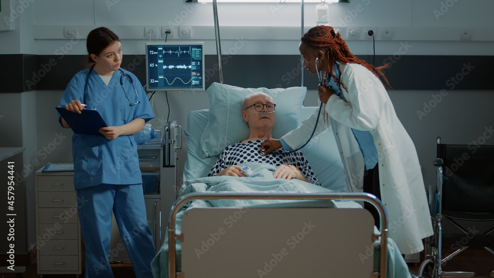 Obraz premium Multi ethnic personnel treats patient in hospital ward at medical clinic. Sick old man receiving modern treatment with nasal oxygen tube and IV drip bag from nurse and doctor at facility