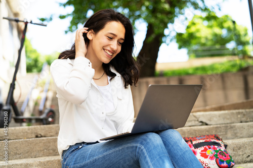 Young businesswoman sitting on steps outdoors and working on laptop. Beautiful girl learning in the park.