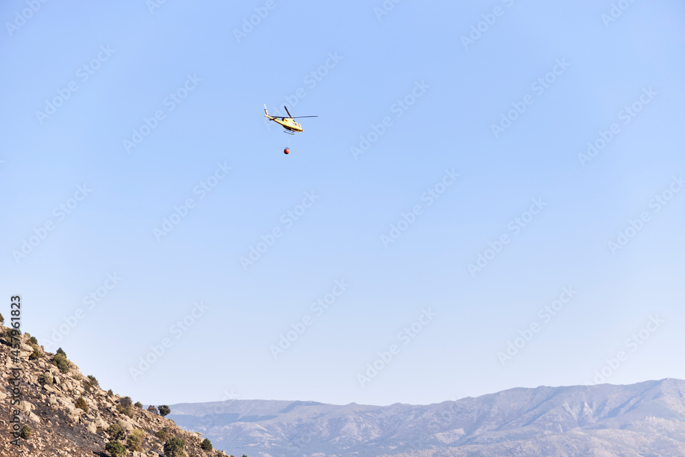 Firefighting helicopter transporting water to extinguish a forest fire. Hazard concept