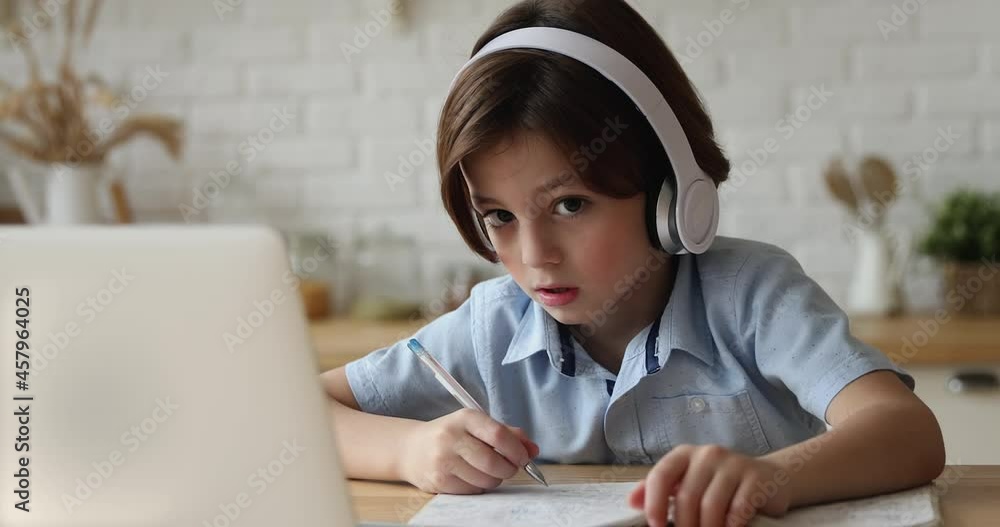 Concentrated little 7s kid boy wearing wireless headphones listening educational lecture in online school, attending virtual classroom lesson, communicating distantly with teacher, e-learning concept. Concentrated little 7s kid boy wearing wireless headphones listening educational lecture in online school, attending virtual classroom lesson, communicating distantly with teacher, e-learning concept.