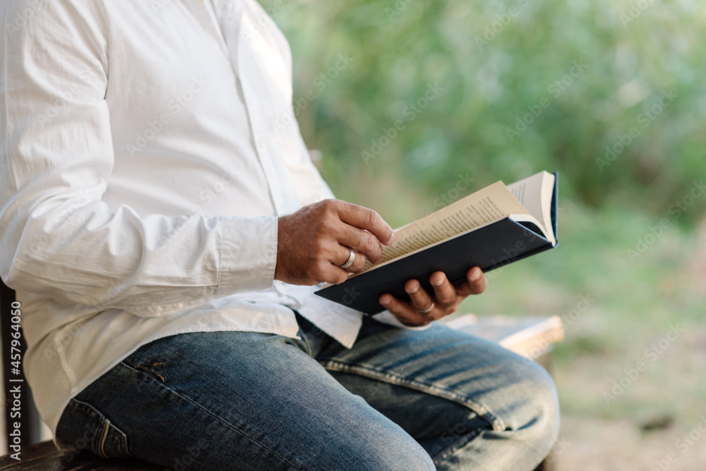 Close up view of a man enjoying free time reading a book while sitting on a bench in the park. Hobby concept. Close up view of a man enjoying free time reading a book while sitting on a bench in the park. Hobby concept.