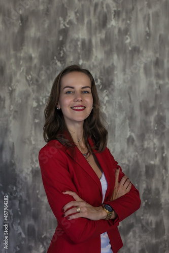 Portrait of a beautiful young business woman with brown hair in a red jacket. Side view of happy smiling girl with red lips on gray background with copy space. The concept of business and success. © pijav4uk
