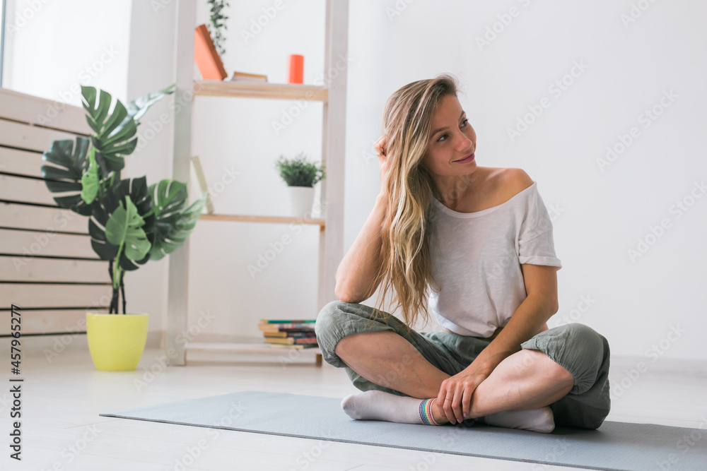 Positive girl sitting on fitness mat resting after pilates or yoga practice. Mindfulness and wellbeing concept. Positive girl sitting on fitness mat resting after pilates or yoga practice. Mindfulness and wellbeing concept.