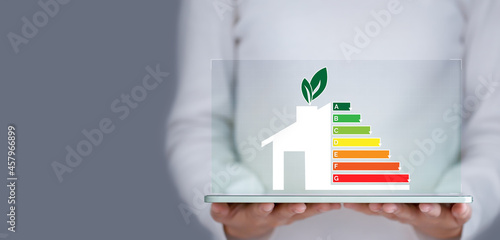 Energy efficiency and green energy concept, woman hand holding tablet and looking at house efficiency rating.