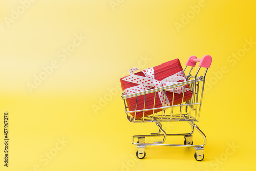 Red gift box in shopping trolley over yellow background