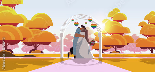 newlywed lesbian couple with flowers kissing near wedding arch transgender love LGBT community wedding celebration