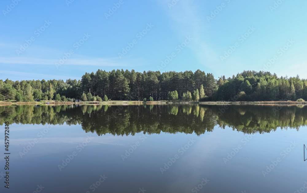 Summer landscape with lake, grass, woods, blue sky in daytime.