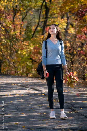 Beautiful girl is walking along the alley of the autumn park. Young thoughtful woman in the forest. Vertical frame
