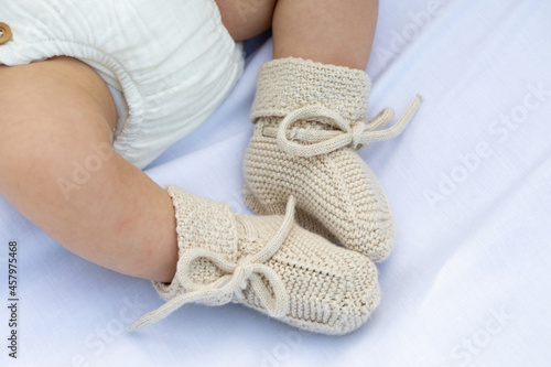 Small little feet from a baby with bootees beige and white colors. Closeup.