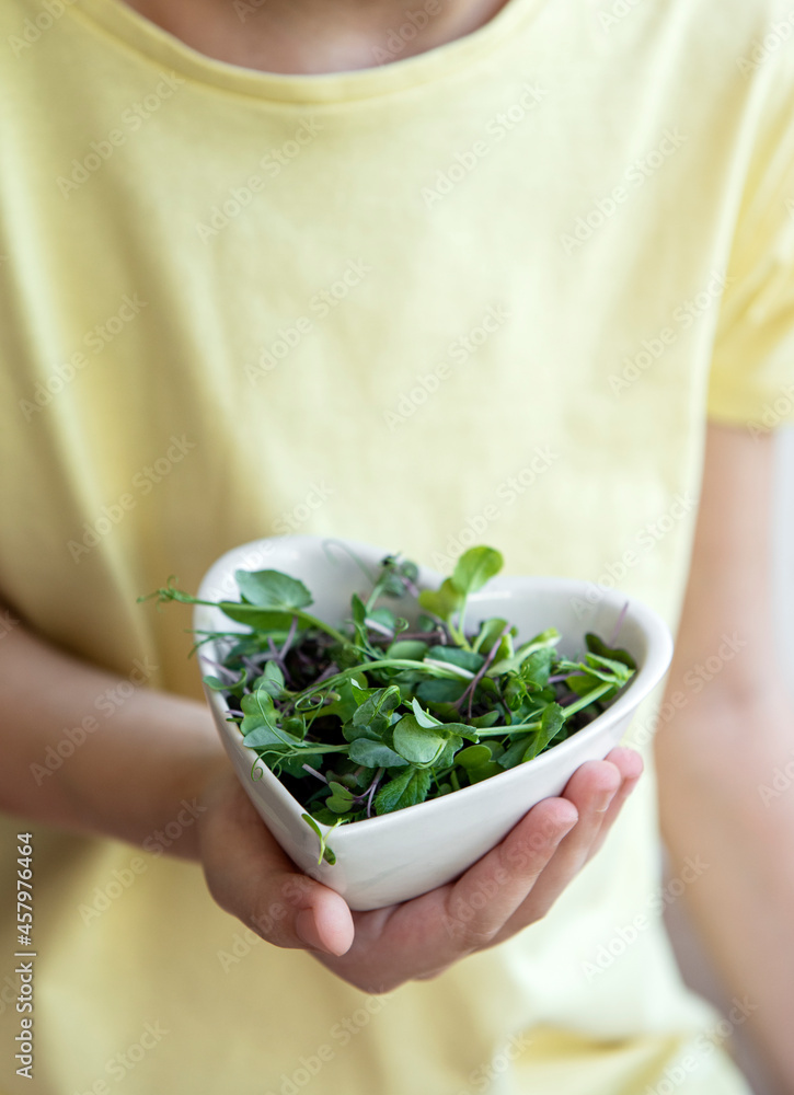 Little girl holding a bowl with microgreens in her hands