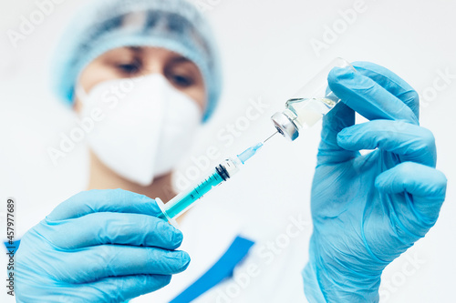A female doctor in a medical face mask and gloves dials the vaccine into a syringe from an ampoule. Medical worker close-up. Vaccination against infectious and colds.