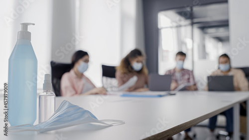 Protective mask and sanitizer on office desk with business people on background