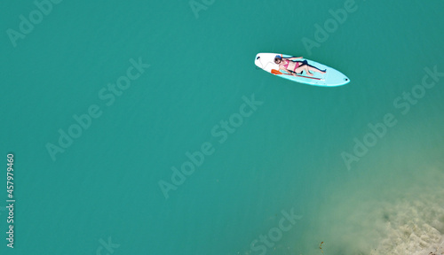 A girl in a dress floats on a glanders board on a pond with bright turquoise water. Warm summer day for travel. Top view from a quadcopter. Aerial photography © Sergei Malkov