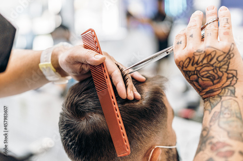 Tattooed hands of a barber cutting the hair of a client