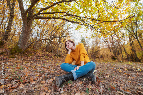 Woman hiking looking at scenic view of autumn foliage mountain landscape. Outdoor adventure travel lady sitting relaxing in nature in autumn season.