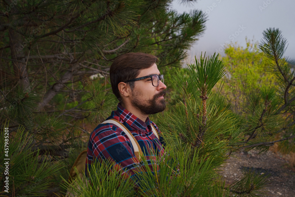 Male hipster Traveler with backpack in plaid shirt and jeans hiking in the mountains travel, trekking in autumn countryside. among the green pines