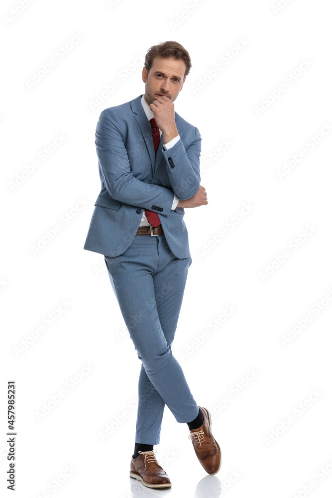 thoughtful young man in blue suit crossing arms and touching chin thoughtful young man in blue suit crossing arms and touching chin