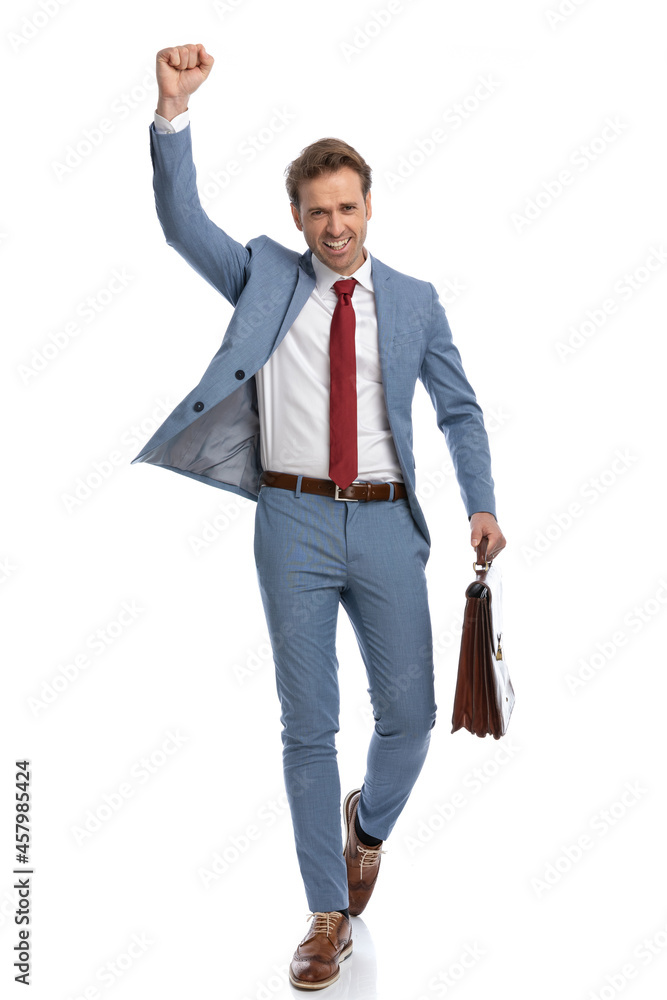 excited young businessman with arm up holding suitcase and celebrating