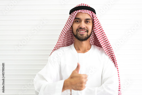 Portrait of happy smiling handsome middle eastern arab man in traditional clothing standing on white wall background photo