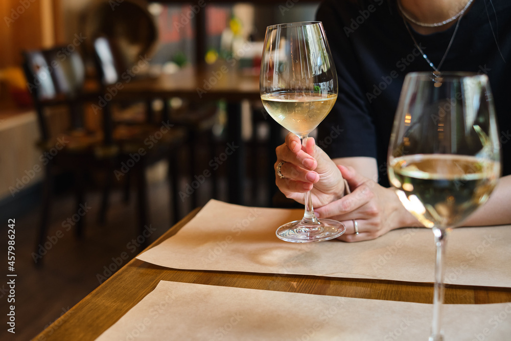 A glass of white wine in the hands of a girl relaxing in a restaurant. Tasting of alcoholic beverages. Summer rest. Romantic evening aperitif. Close-up of a glass of wine. Enjoy the moment