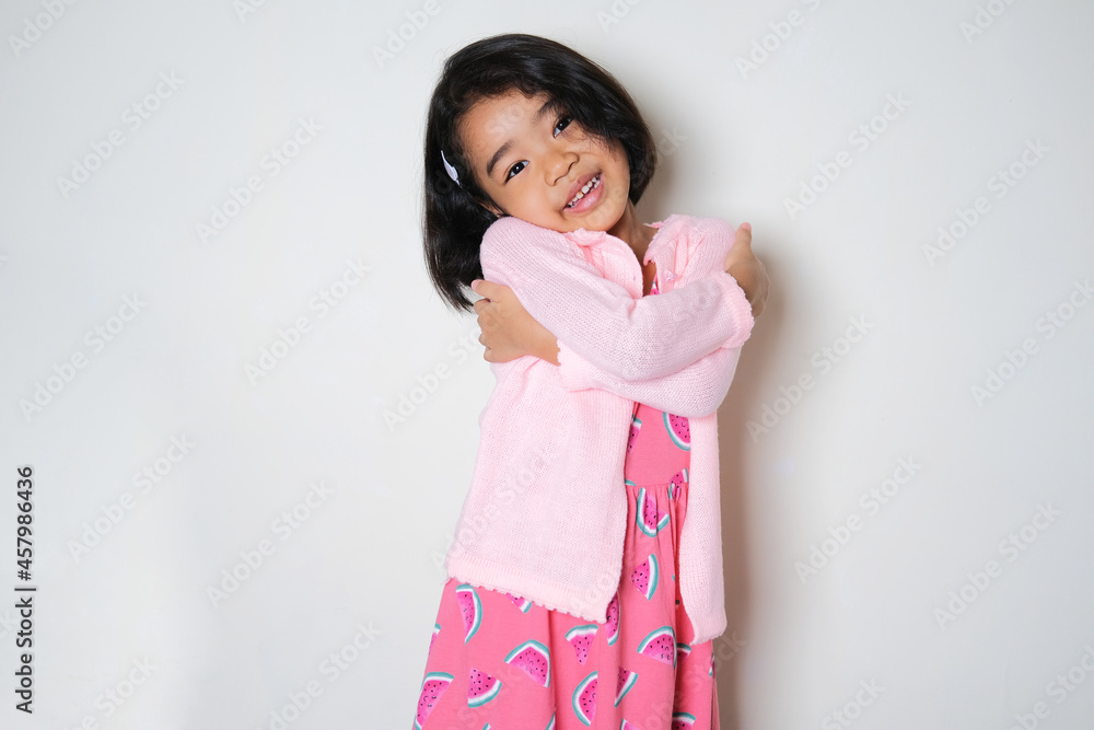 Asian little girl hugging her self and showing happy face expression Asian little girl hugging her self and showing happy face expression