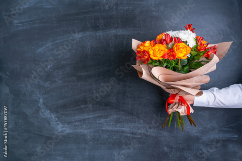 A bouquet of flowers in paper wrapping paper in a man's hand on the background of a chalk board. Copy space