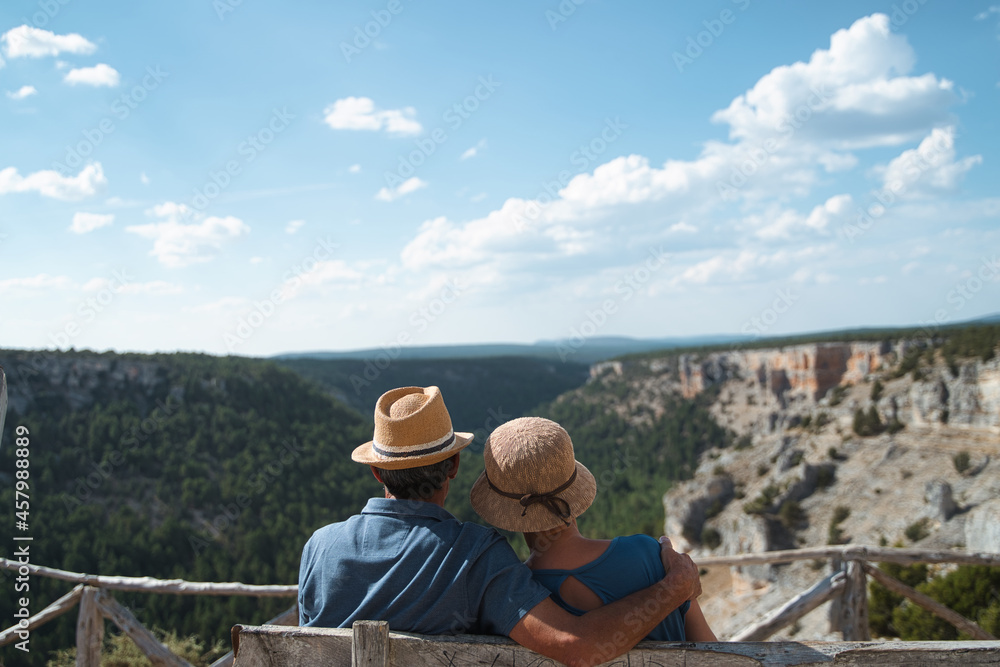 Unrecognizable older couple in hats embracing on a bench overlooking a national park.