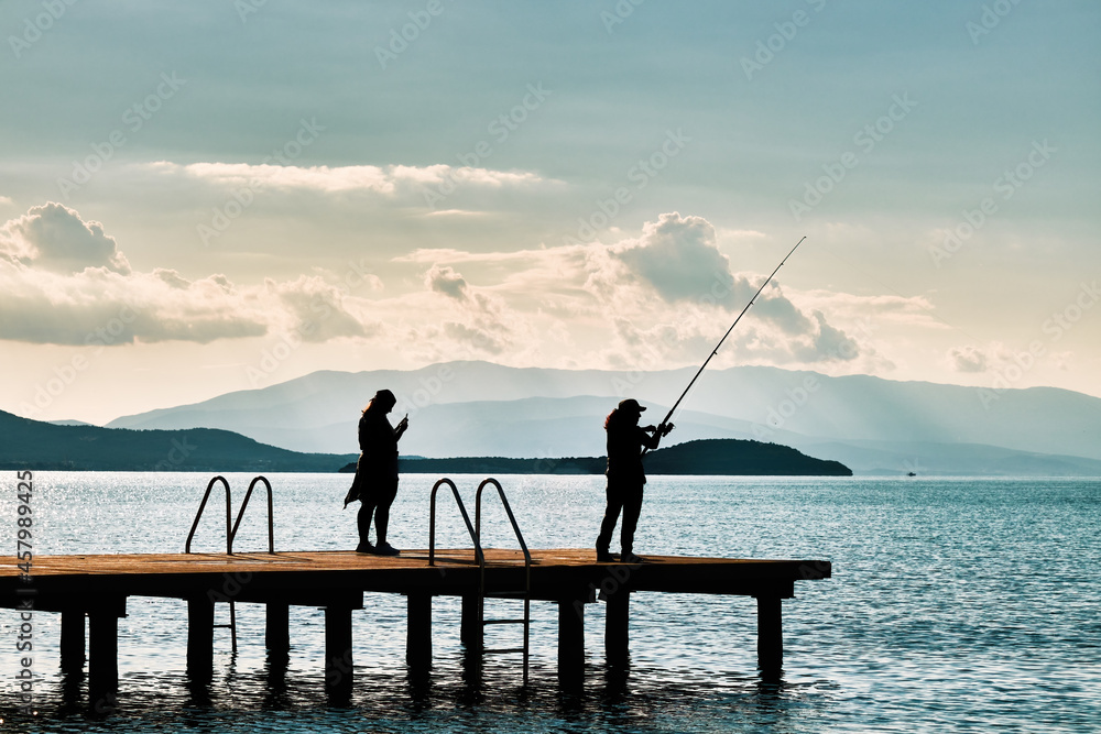 Silhouette of a woman catching fish with a fishing rod on the pier