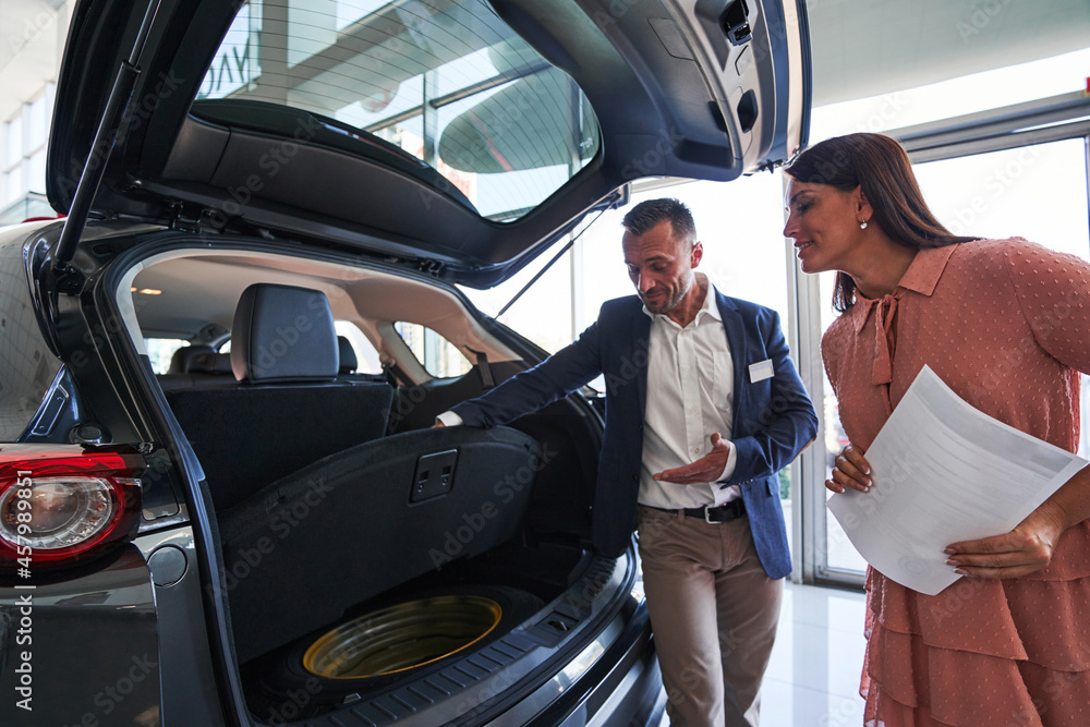 Curious lady looking at the car trunk and smiling Curious lady looking at the car trunk and smiling
