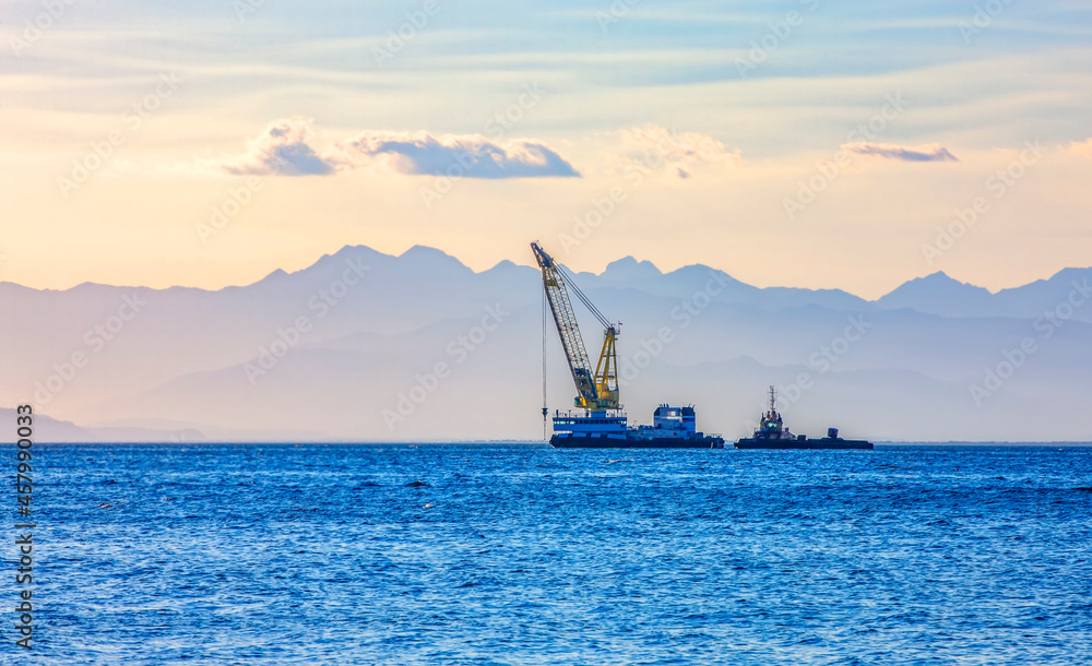 sea ship with a crane on the background of a mountain range in the haze