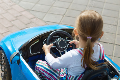 A baby girl is having fun riding a blue electric car in an amusement park. A Cute Little Girl Drives A Children's Car. The concept of a happy childhood. Entertainment for children. Street toys.
