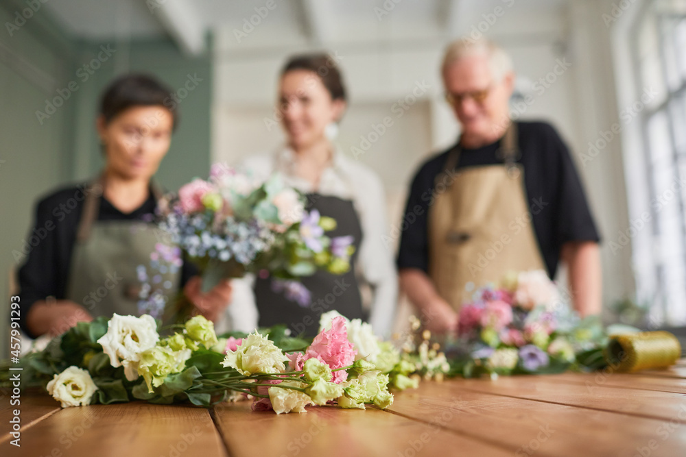 Portrait of three florists arraigning flower compositions on wooden table in cozy workshop, focus non foreground, copy space Portrait of three florists arraigning flower compositions on wooden table in cozy workshop, focus non foreground, copy space
