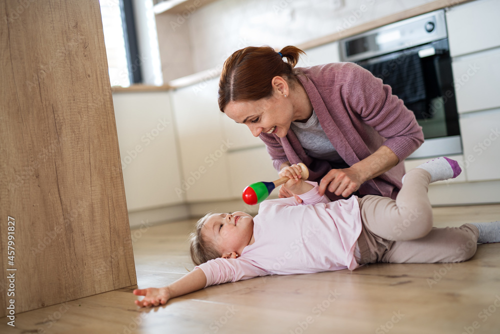 Naklejka premium Happy mother with small daughter playing indoors in kitchen, laughing.