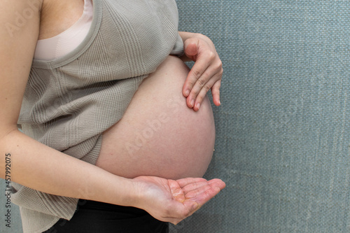 A young pregnant Asian woman applying body lotion not to make pregnancy stretch mark photo