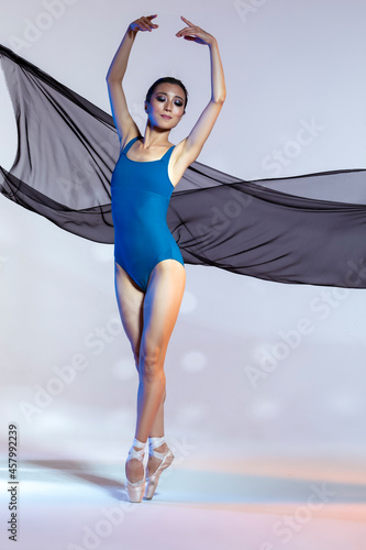 Classical Ballet Ideas. Young Japanese Female Ballet Dancer Dancing With Flying Black Cloth While Posing in Blue Bodysuit Against White Background With Pattern