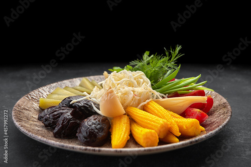 Pickled vegetables on a dark background cucumbers tomatoes herbs