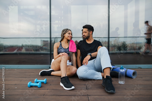 Young couple in love resting after exercise outdoors on terrace, sport and healthy lifestyle concept.
