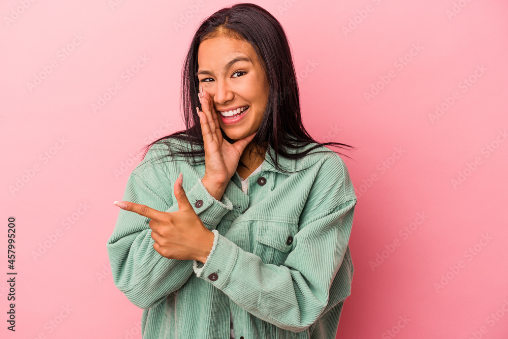 Young latin woman isolated on pink background  saying a gossip, pointing to side reporting something.