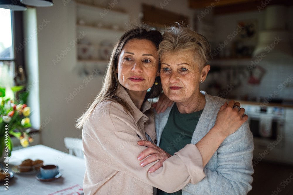 Portrait of senior mother hugging with adult daughter indoors at home, looking aside. Portrait of senior mother hugging with adult daughter indoors at home, looking aside.