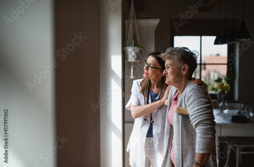 Side view of healthcare worker or caregiver visiting senior woman indoors at home, helping her to walk.