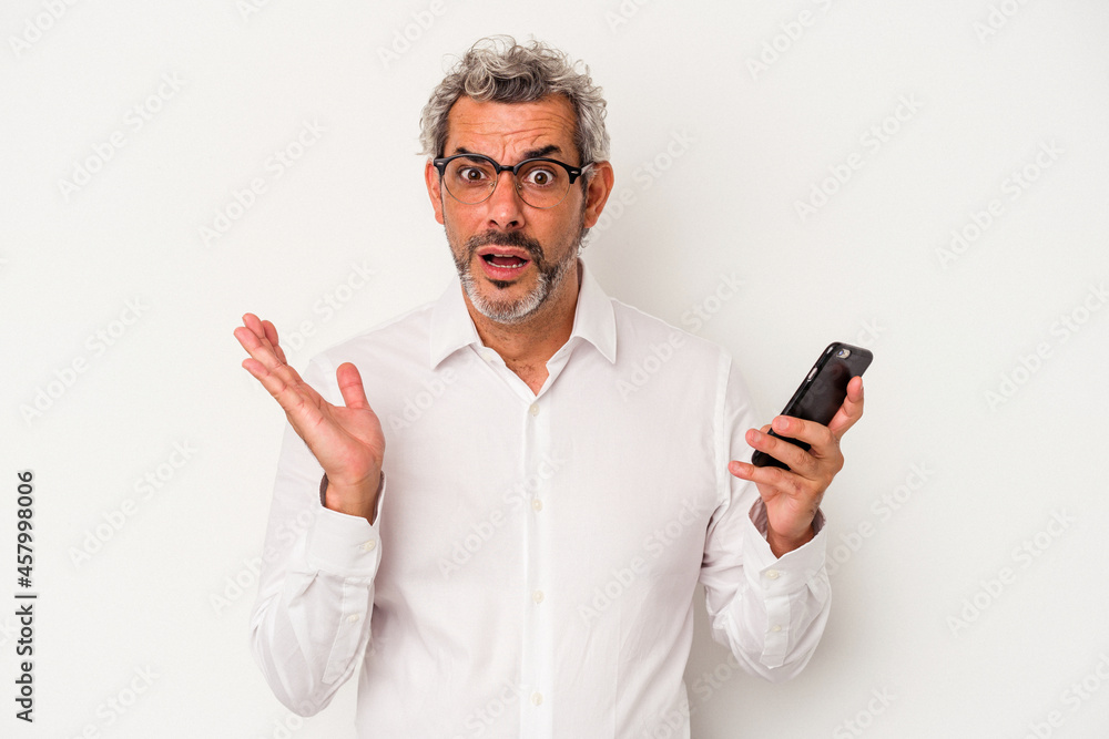 Middle age caucasian business man holding a mobile phone isolated on white background surprised and shocked. Middle age caucasian business man holding a mobile phone isolated on white background surprised and shocked.