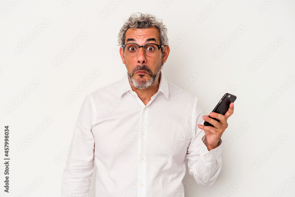 Middle age caucasian business man holding a mobile phone isolated on white background shrugs shoulders and open eyes confused. Middle age caucasian business man holding a mobile phone isolated on white background shrugs shoulders and open eyes confused.