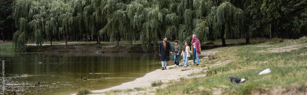 Muslim family walking near lake in park, banner