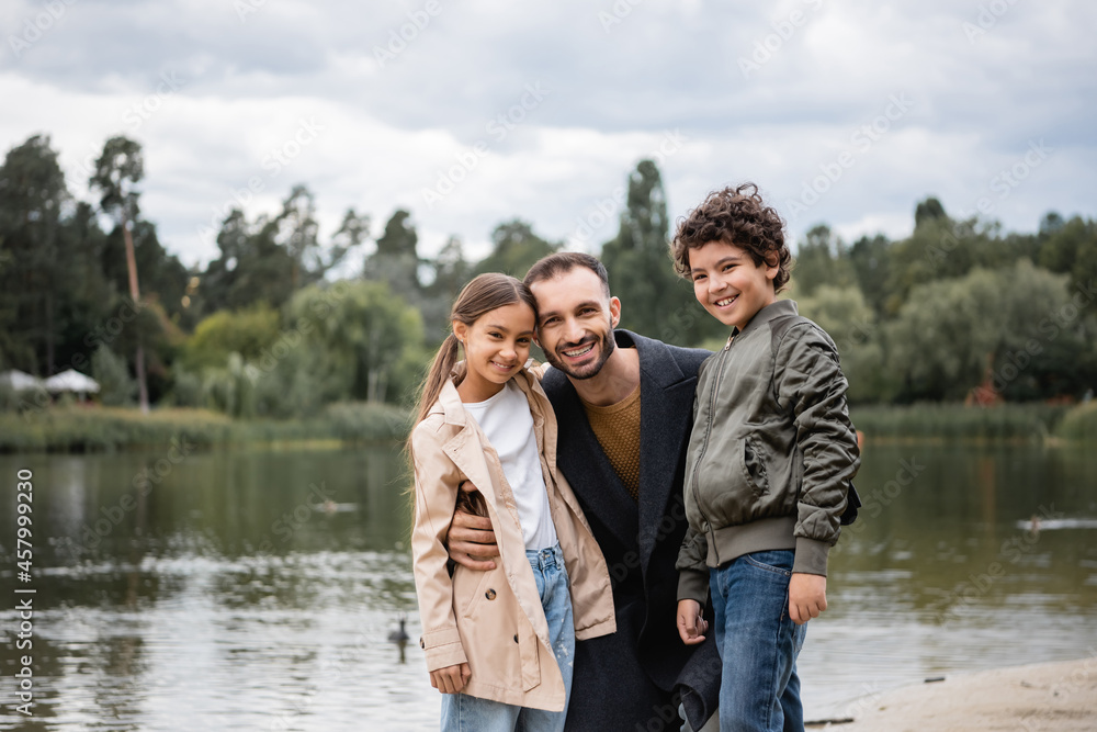 Smiling muslim father hugging children near lake