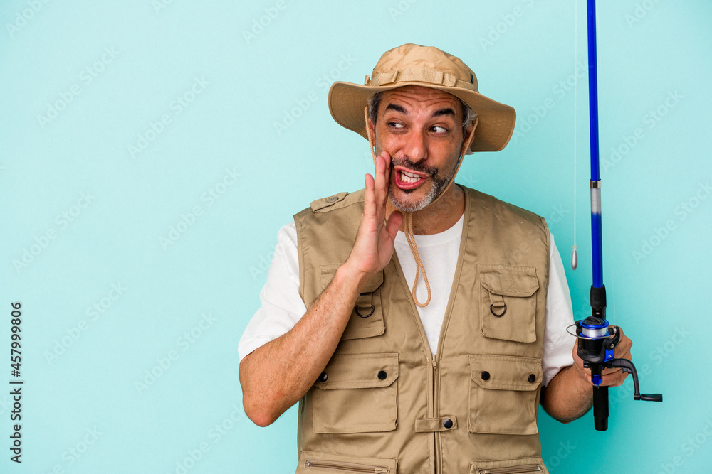 Fototapeta premium Middle age caucasian fisherman holding rod isolated on blue background is saying a secret hot braking news and looking aside