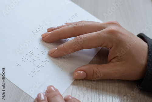 Close-up woman reads the text to the blind. Woman's hands on paper with braille code.